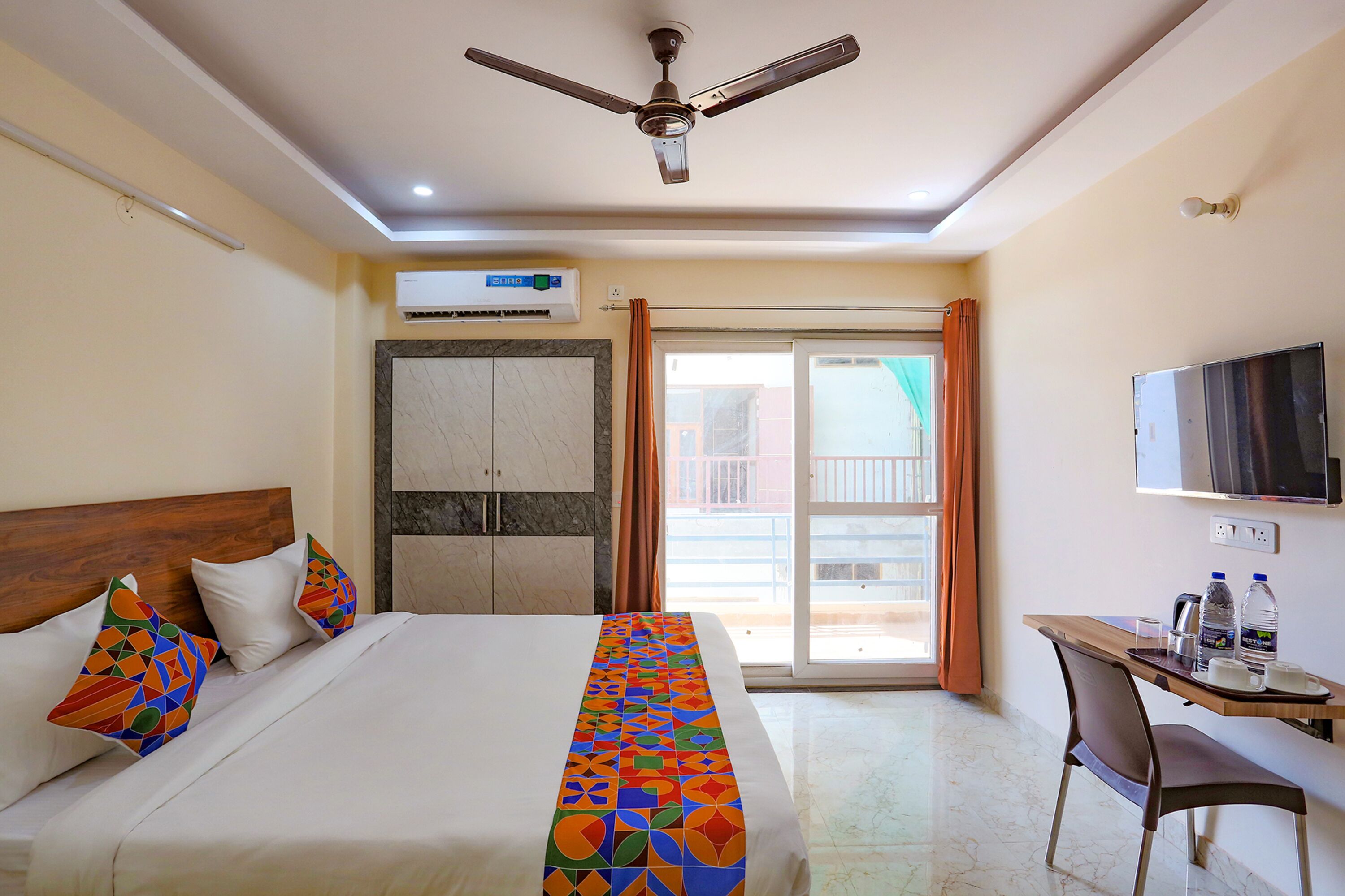 A hotel room with a bed, a desk, a chair, a TV, and a balcony with curtains.