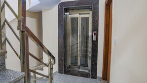 Een hotellift met een digitaal scherm, een marmeren vloer en een houten deurkozijn.