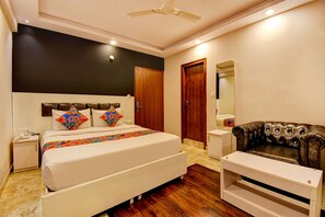 A bedroom with a bed, a nightstand, a dresser, a leather armchair, and a ceiling fan. - FabHotel Cozzy Inn - Jayanagar (Bengaluru)