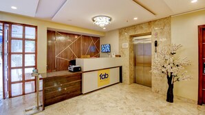 A hotel reception area with a reception desk, a television, an elevator, and a vase with flowers. - FabHotel Cozzy Inn - Jayanagar (Bengaluru)