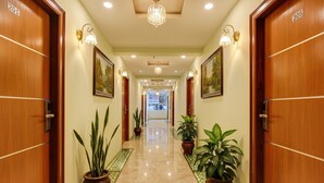 A hotel hallway with wooden doors numbered 201 and 205, potted plants, and wall-mounted light fixtures. - FabHotel Cozzy Inn - Jayanagar (Bengaluru)