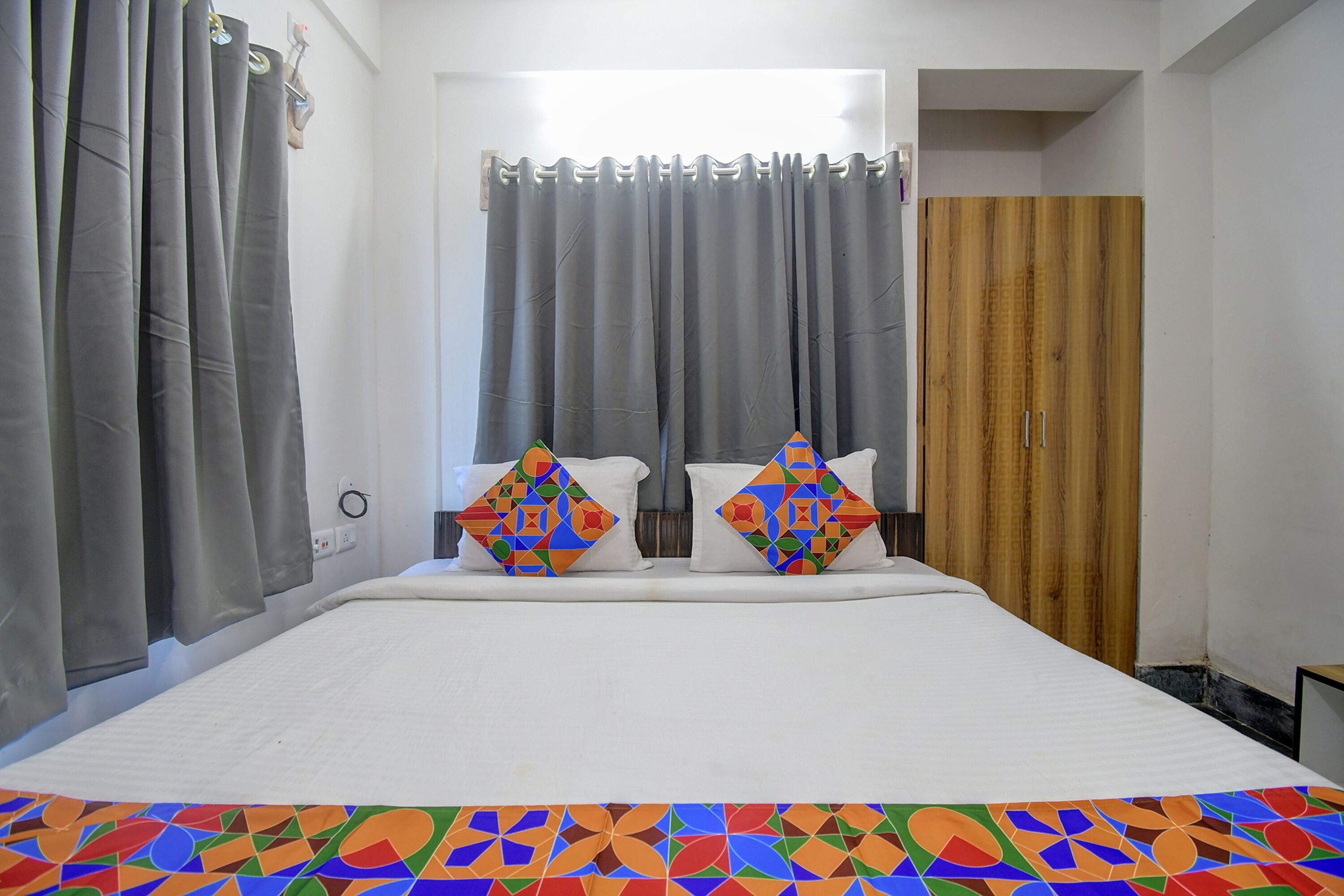 A bedroom with a bed, two pillows, a wooden wardrobe, and grey curtains.