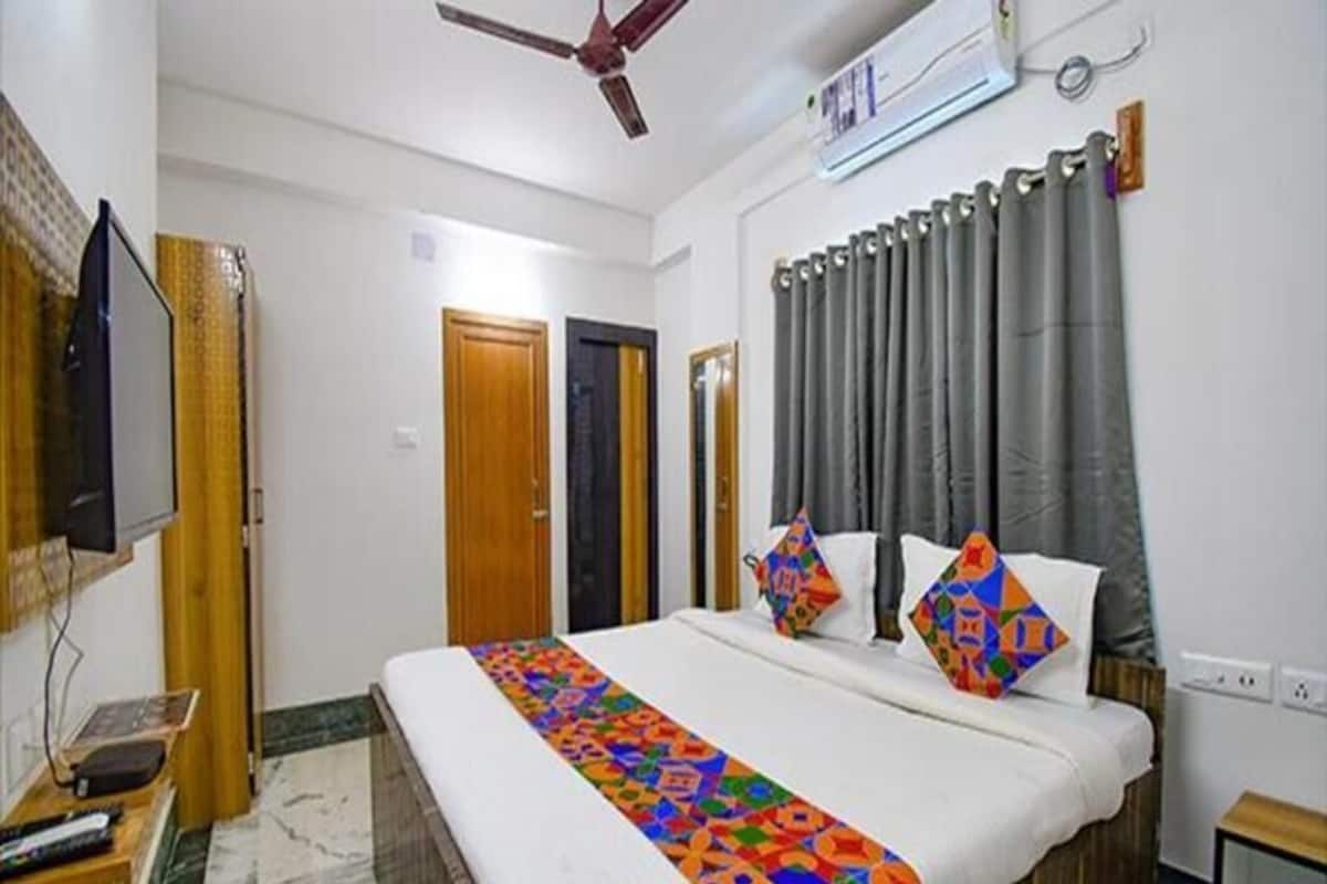 Une chambre d’hôtel équipée d’un lit, d’une télévision, d’un ventilateur de plafond et d’une fenêtre avec des rideaux.