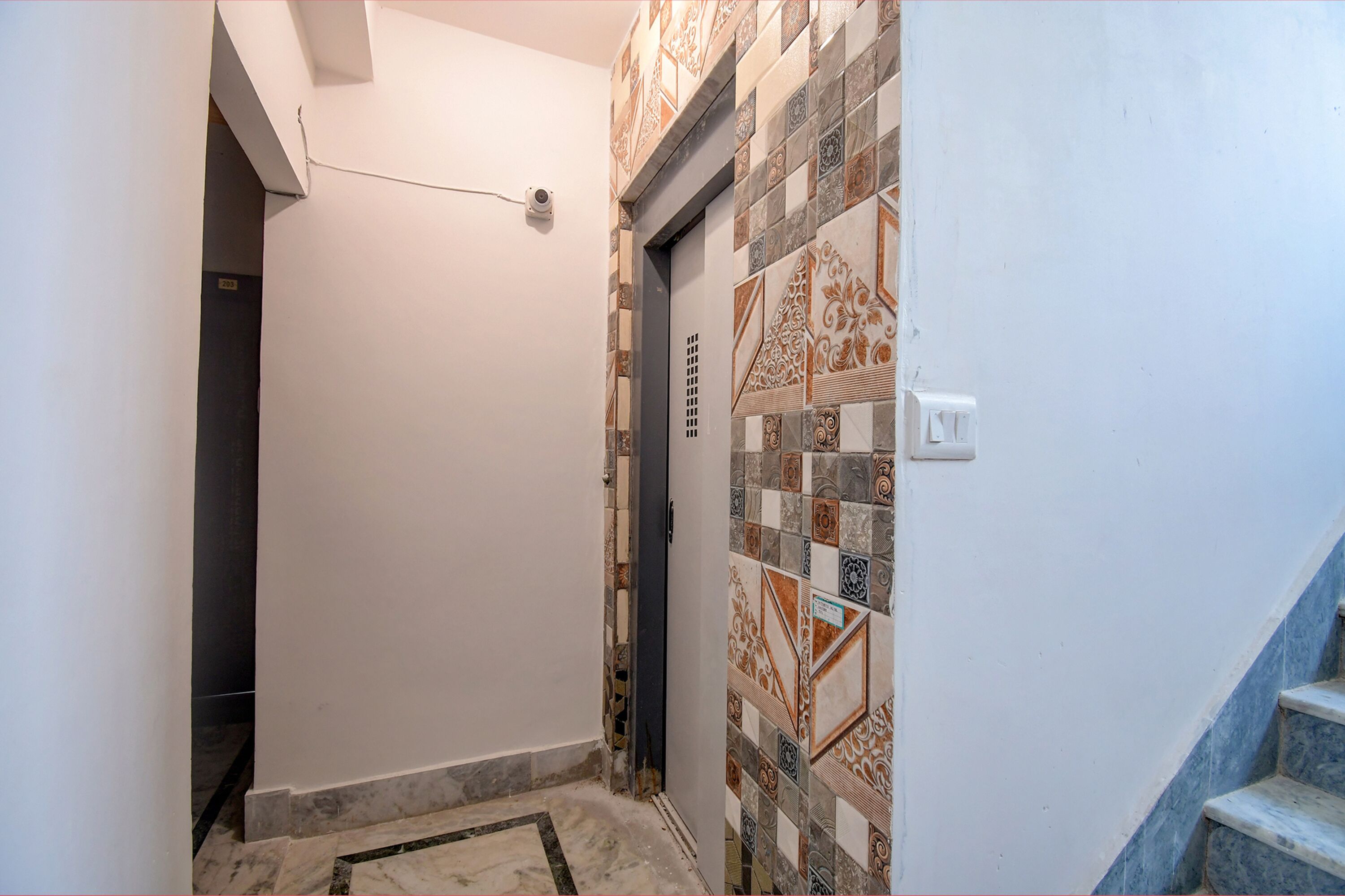 Un estrecho pasillo con pared de azulejos, una puerta y suelo de mármol.