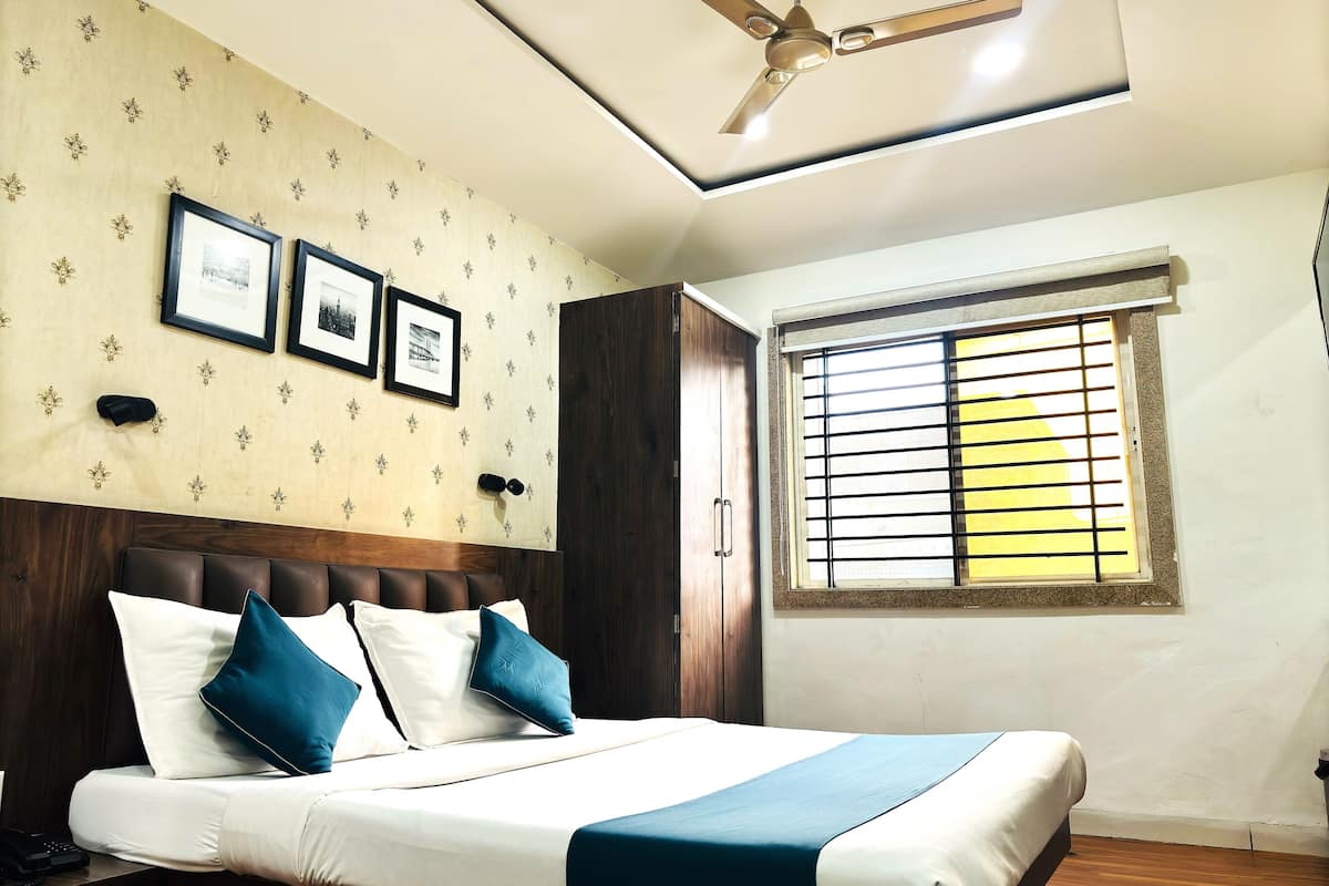 A hotel room with a bed, a ceiling fan, a window with blinds, and framed pictures on the wall.