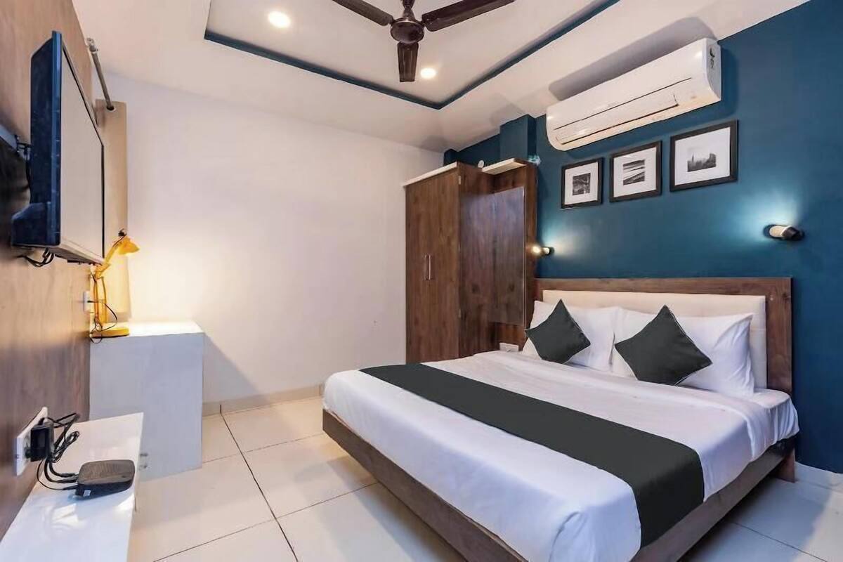 A bedroom with a bed, a ceiling fan, an air conditioning unit, a bedside table, and a wall-mounted TV.