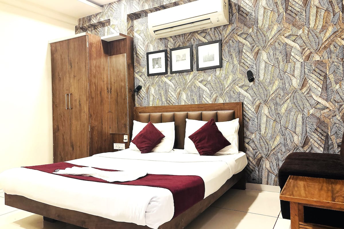 A neatly arranged bedroom with a bed, wooden wardrobe, and patterned wallpaper.