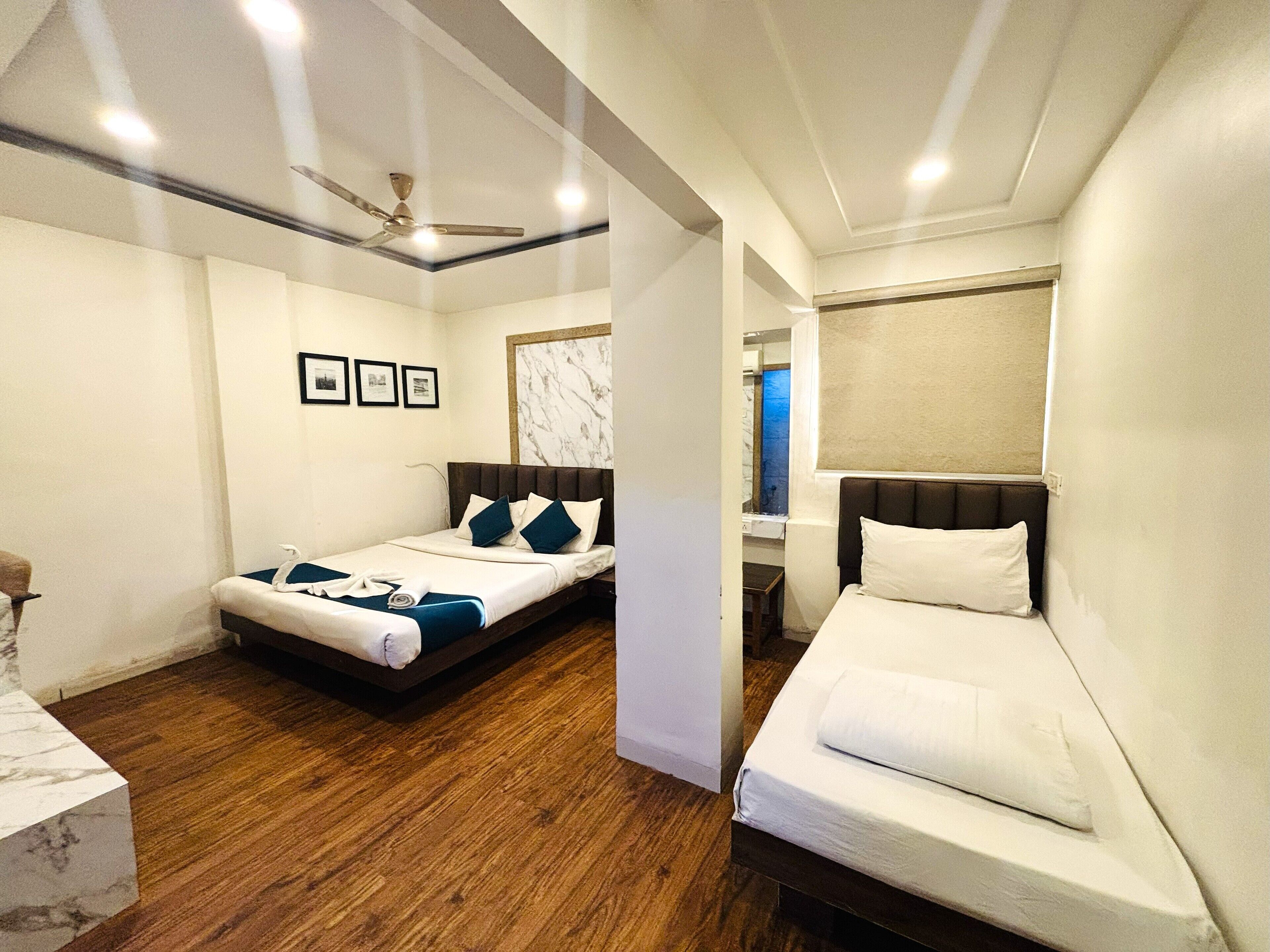 Una habitación de hotel con dos camas, suelo de madera, ventilador de techo y cuadros enmarcados en la pared.