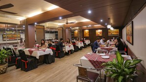 A restaurant with multiple tables, chairs, and potted plants. - Fabhotel Surya (Bhopal)