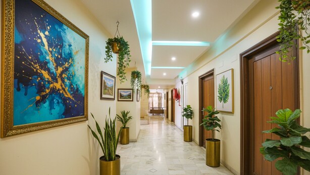 A hotel hallway with a large abstract painting, potted plants, and framed pictures on the walls. - Fabhotel Surya (Bhopal)