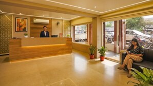 A hotel reception area with a wooden reception desk, a receptionist, and a waiting area with a sofa and potted plants. - Fabhotel Surya (Bhopal)