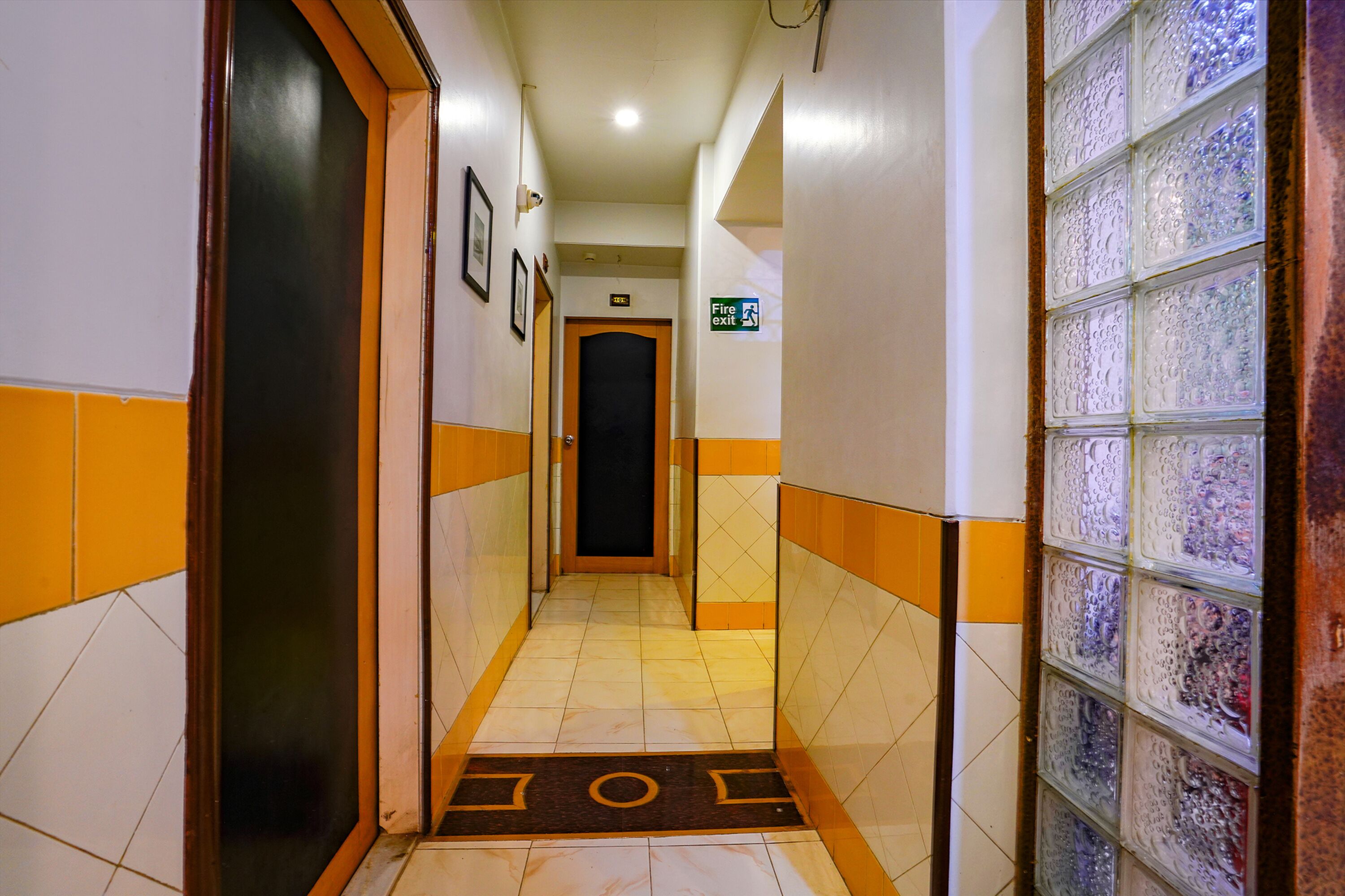 A hotel hallway with a tiled floor, a fire exit sign, and a door at the end.