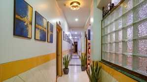 Un couloir d’hôtel aux murs recouverts de carreaux, au sol orné de motifs, agrémenté de plantes en pot et décoré d’œuvres d’art encadrées.