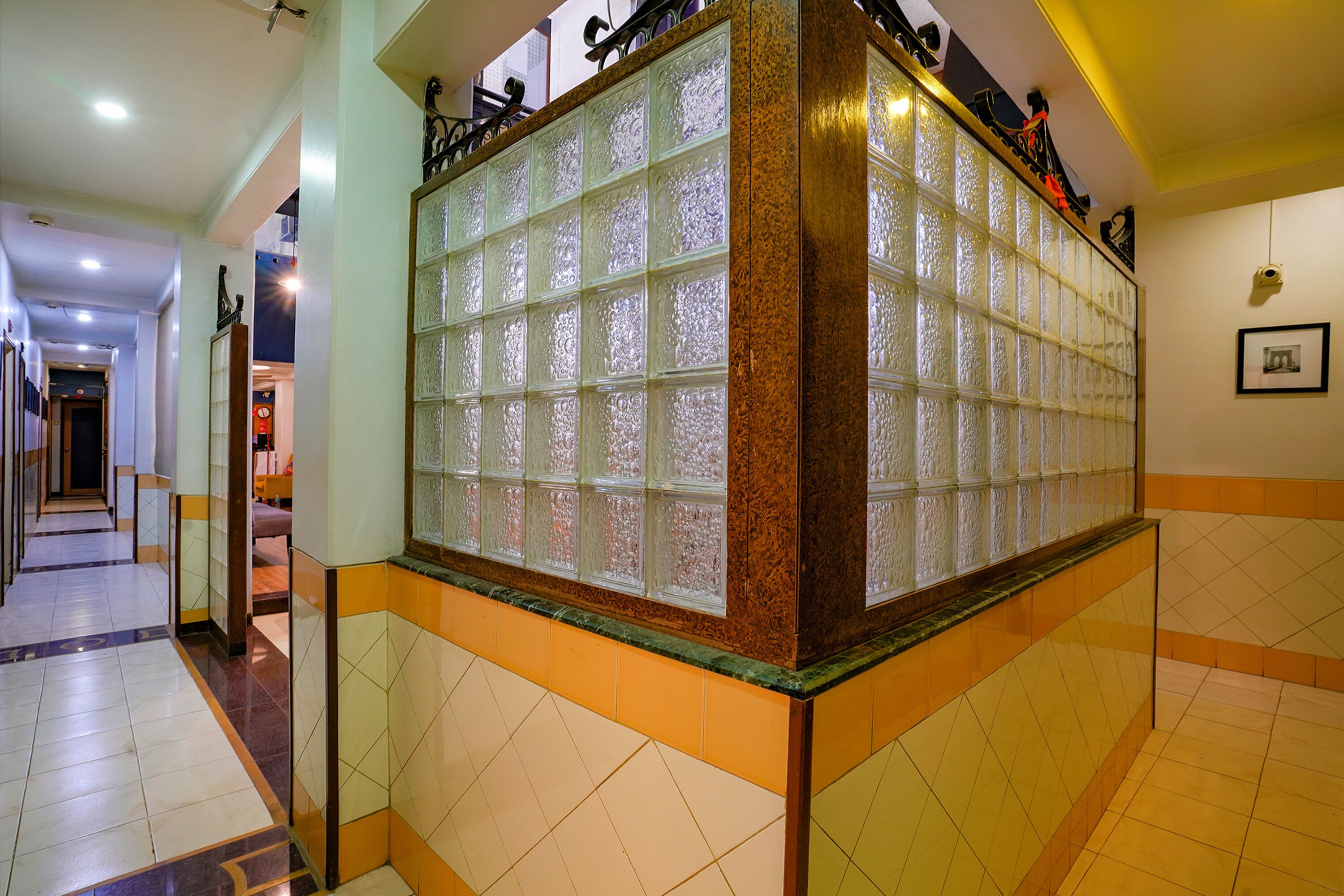 Un hall d’hôtel doté d’un sol carrelé, d’une cloison en verre ornée de panneaux décoratifs et d’un escalier menant à un étage supérieur.
