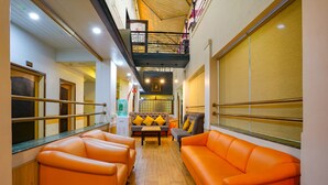 Un hall d’hôtel avec des sièges orange, un escalier et une vue sur la ville.