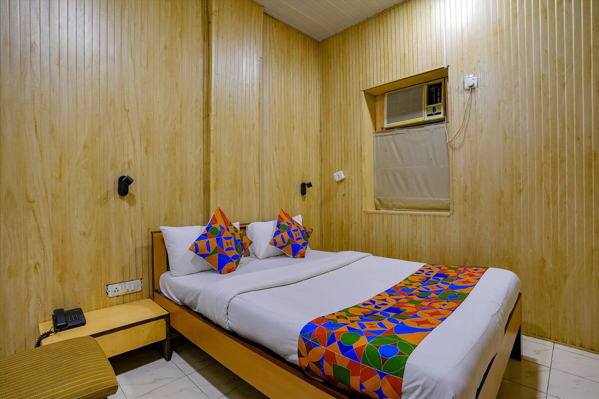 A wooden-paneled room with a bed, a bedside table, and a window.