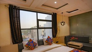A hotel room with a large bed, a sofa, a small table, and a window with curtains. - Fabhotel Sun Park (Bhopal)