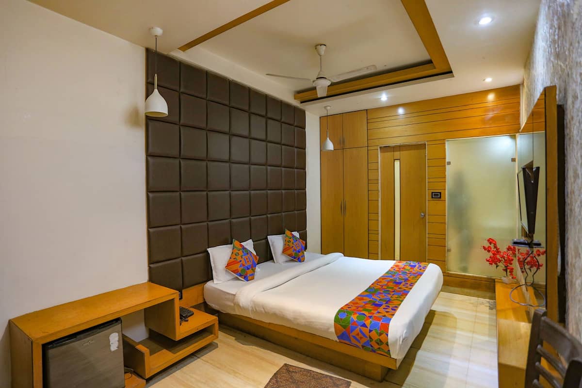Una habitación de hotel moderna con una cama grande, un televisor integrado, una mesita de noche de madera, un ventilador de techo y un armario.