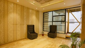 A room with patterned wallpaper, two dark armchairs, a potted plant, and a large window with a view. - Fabhotel Sun Park (Bhopal)