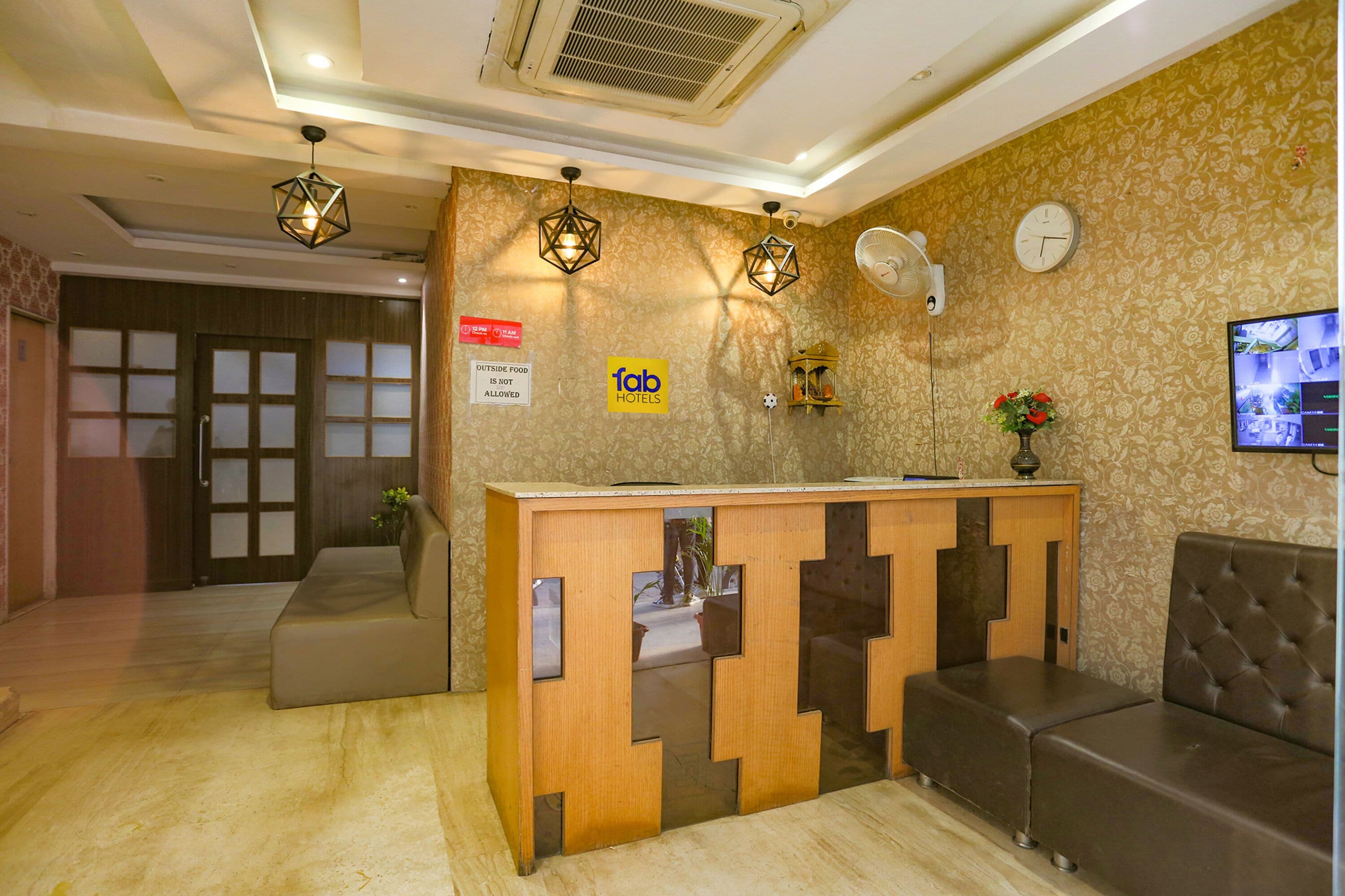 A hotel reception area with a wooden reception desk, a clock, and a wall-mounted TV.
