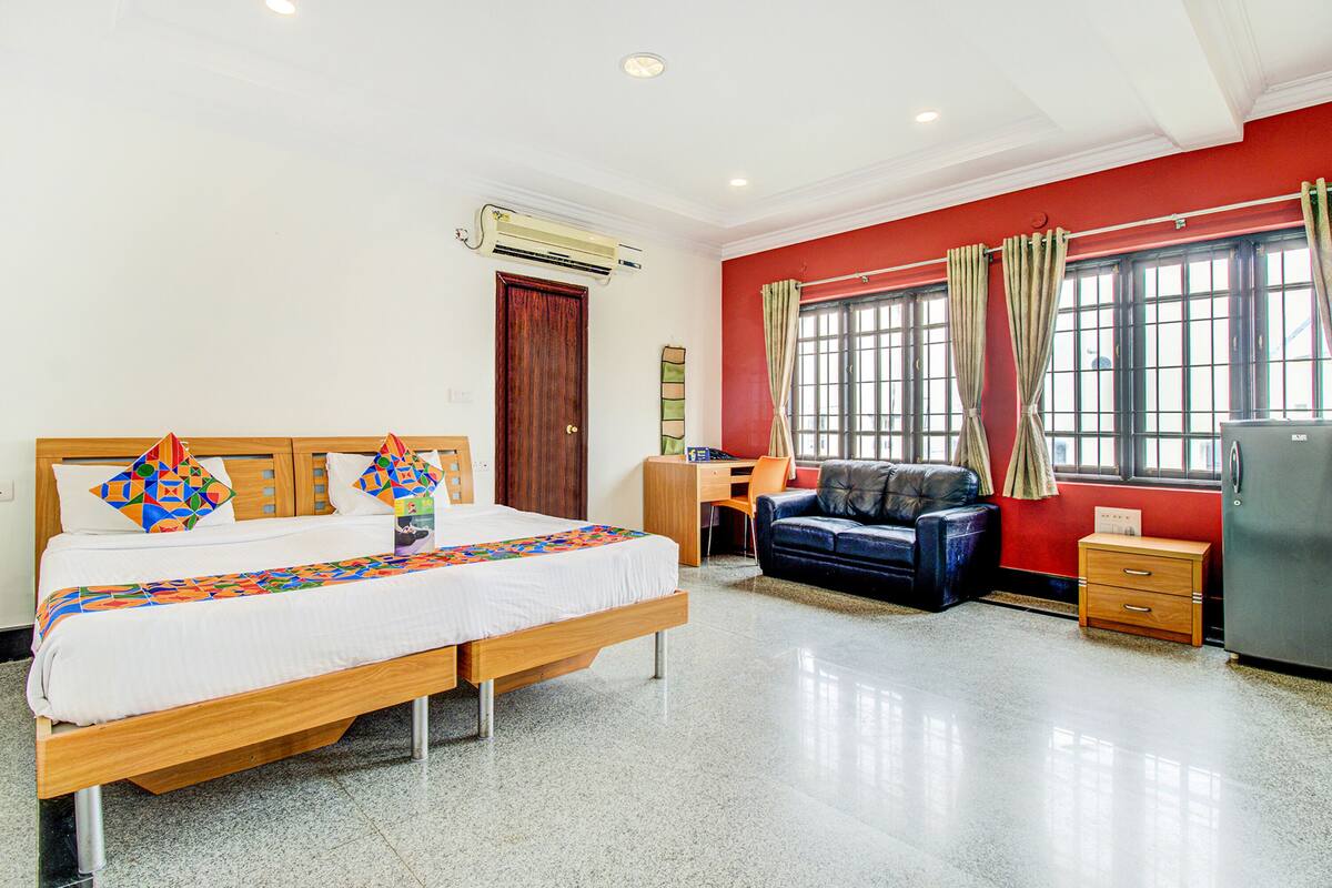 A hotel room with a bed, a desk, a chair, a sofa, and a refrigerator.