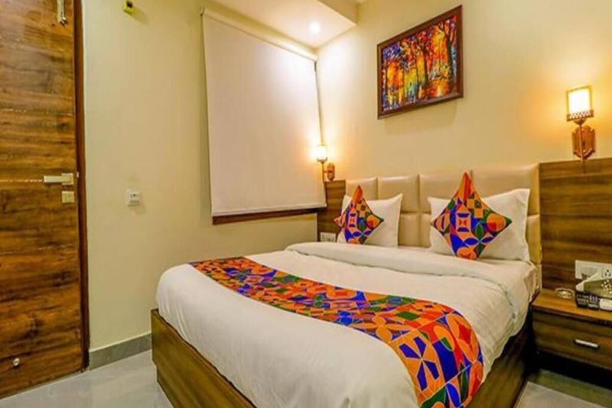 A hotel room with a bed, a nightstand, a wooden door, a wall-mounted artwork, and a window.