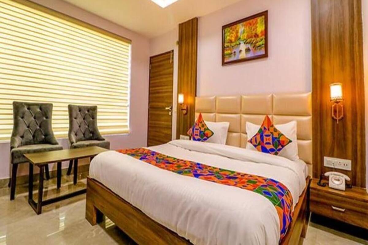 A hotel room with a bed, two chairs, a bedside table, a nightstand, and a painting on the wall.
