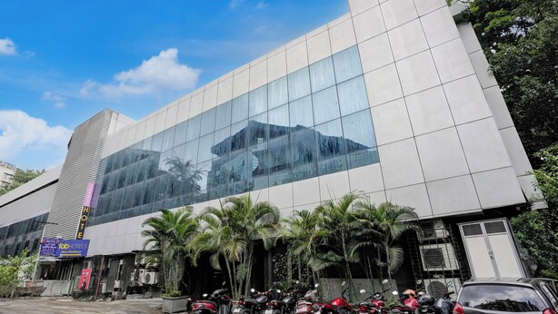 A modern hotel with a reflective glass facade, palm trees, and parked motorcycles. - Veera Residency (Mumbai)