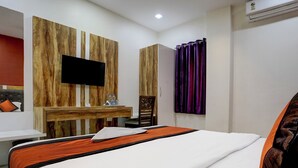 A hotel room with a large bed, a wooden desk, a flat-screen TV mounted on the wall, and a window with purple curtains. - Veera Residency (Mumbai)
