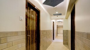A corridor with wooden doors and brick walls, leading to a room with a window. - Veera Residency (Mumbai)