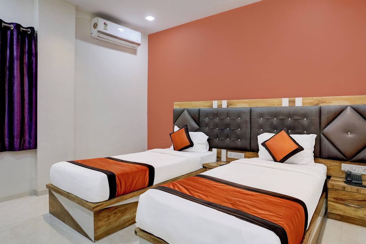 A hotel room with two single beds, a wooden headboard, an air conditioning unit, and a telephone on the nightstand.
