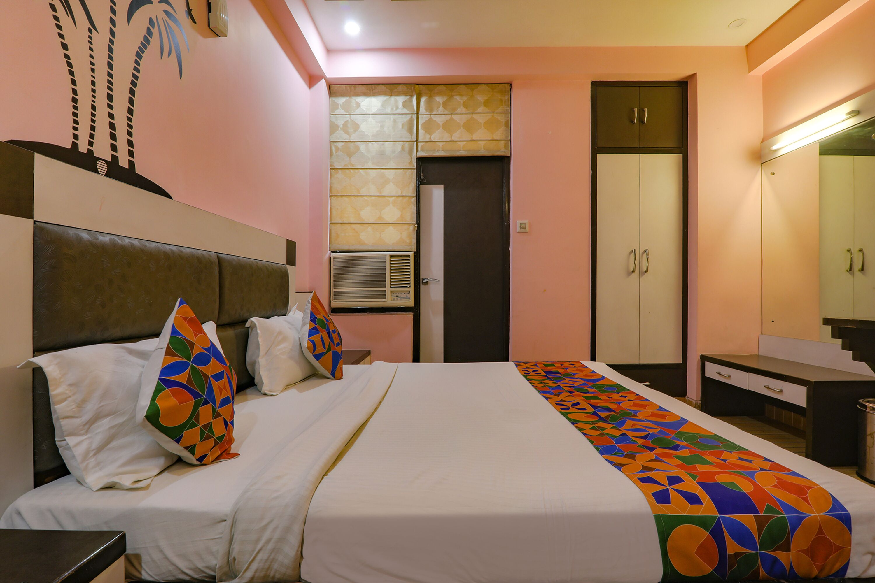 A hotel room with a bed, a nightstand, a dresser, a mirror, and a wardrobe.