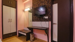 Een kamer met een kast, een bureau, een prullenbak en een aan de muur bevestigde televisie.