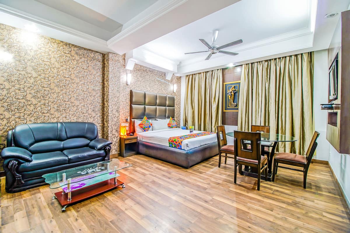 A modern hotel room with a large bed, a sofa, a glass coffee table, and a dining area with chairs.