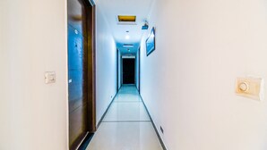 Un couloir étroit et bien éclairé, avec un luminaire au plafond, une porte sur la gauche et un appliques mural sur la droite.