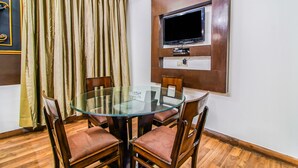 Un coin repas avec une table en verre entourée de chaises en bois, un téléviseur à écran plat fixé au mur et une grande fenêtre avec des rideaux.