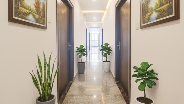 A hallway with two potted plants, a door at the end, and a painting on the wall. - Via Corner Courtyard (Hyderabad)