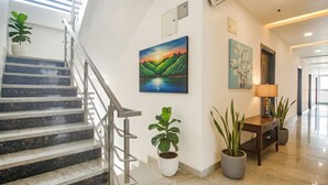 A modern interior with a staircase, a painting of a landscape, and potted plants. - Via Corner Courtyard (Hyderabad)