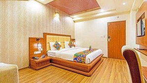 Una camera d'albergo con pavimento in legno, un letto con coperta colorata, un comodino con una lampada e una porta in legno.