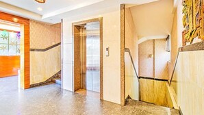 Un'elegante hall moderna con pavimento in marmo, un ascensore in vetro e una scala con corrimano.