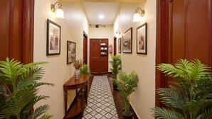 A hallway with wooden doors, framed artwork on the walls, and potted plants. - FabHotel Golden Imperial (Kolkata)