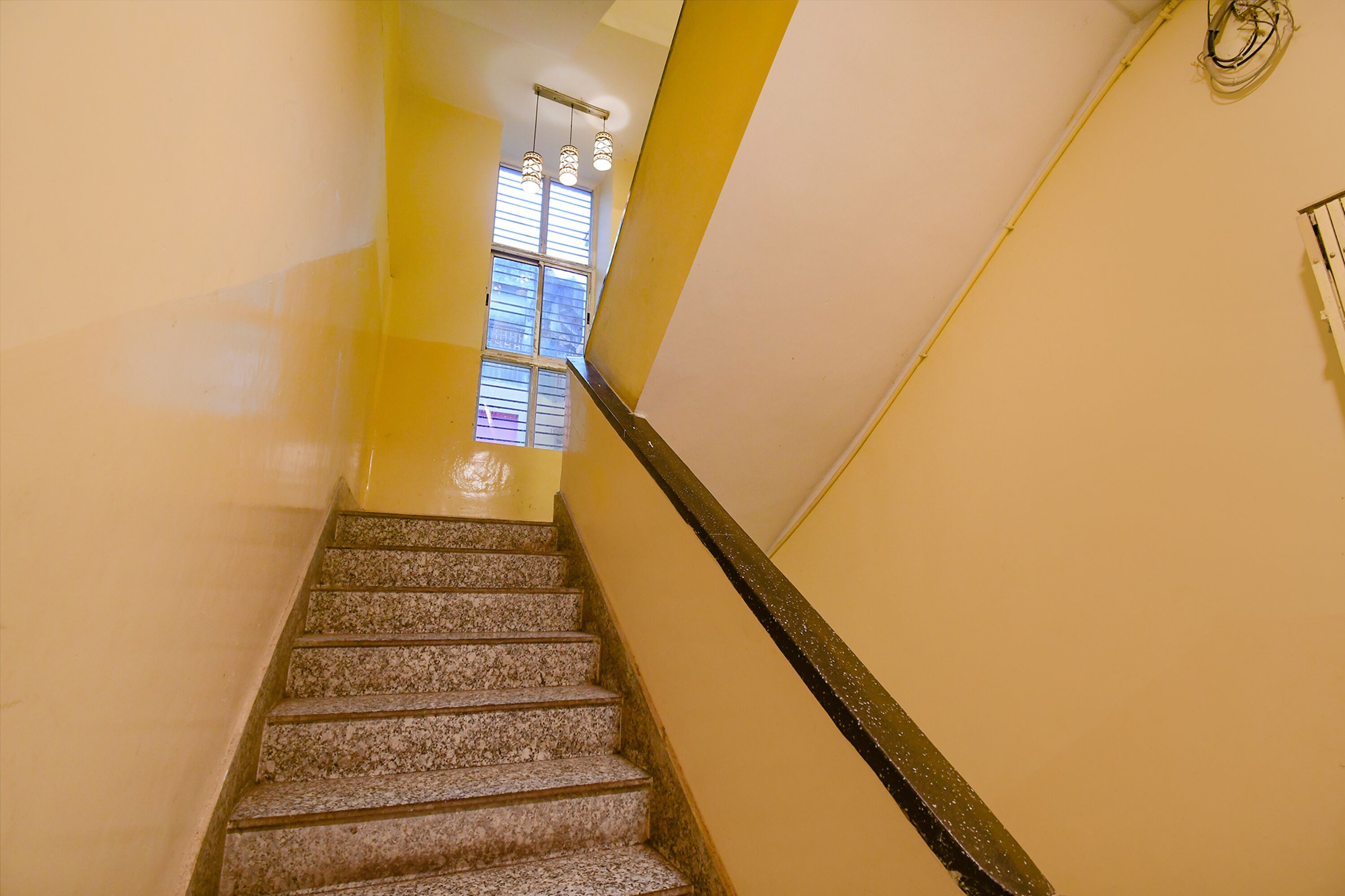 A staircase with a handrail, a window with blinds, and a wall with a light switch.