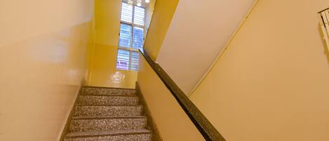 A staircase with a handrail, a window with blinds, and a wall with a light switch.