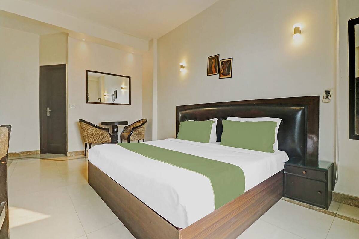A hotel room with a large bed, a bedside table, a chair, a mirror, and wall-mounted lights.