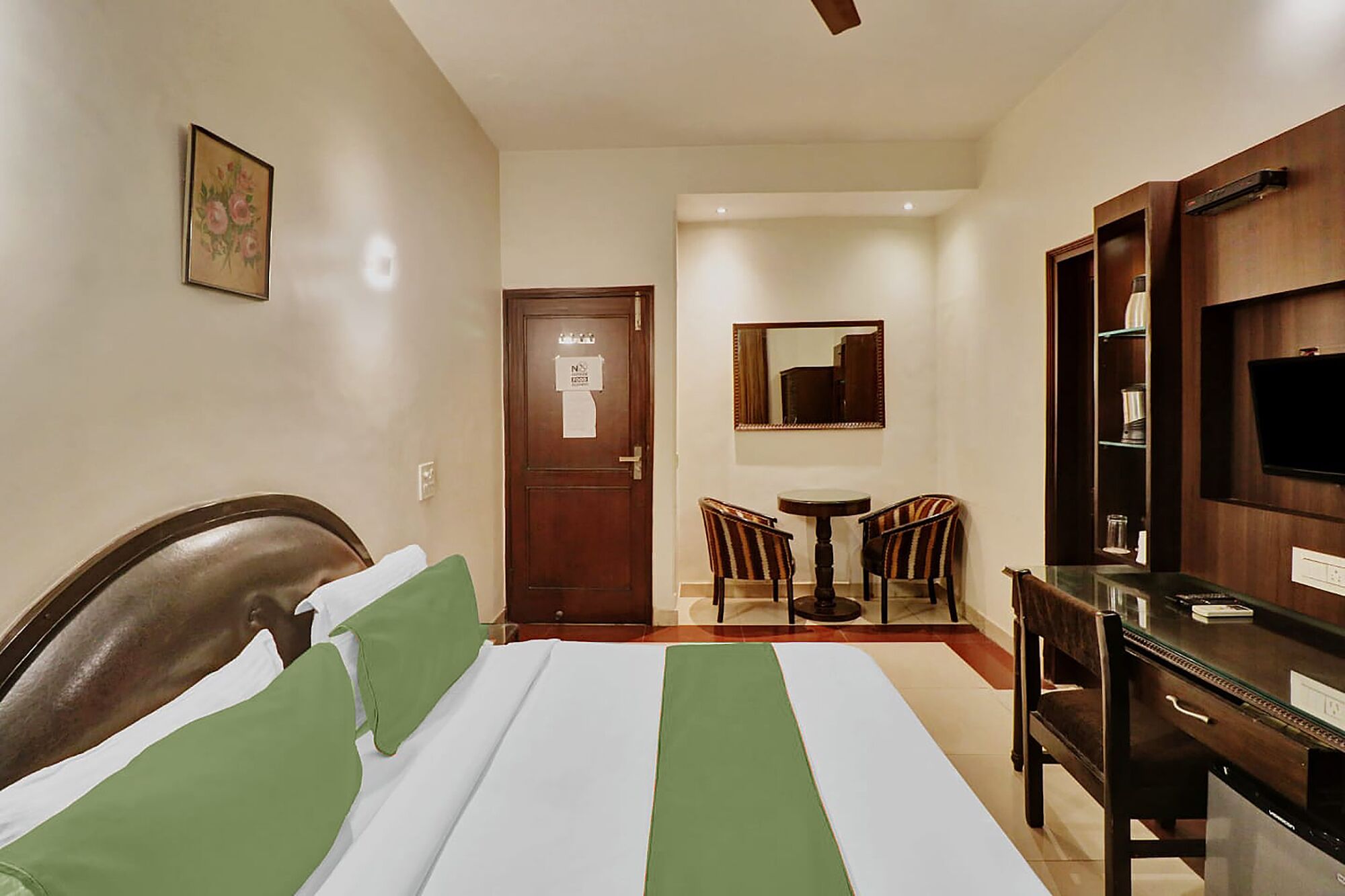 A hotel room with a bed, a desk, a chair, a television, and a door with a sign.