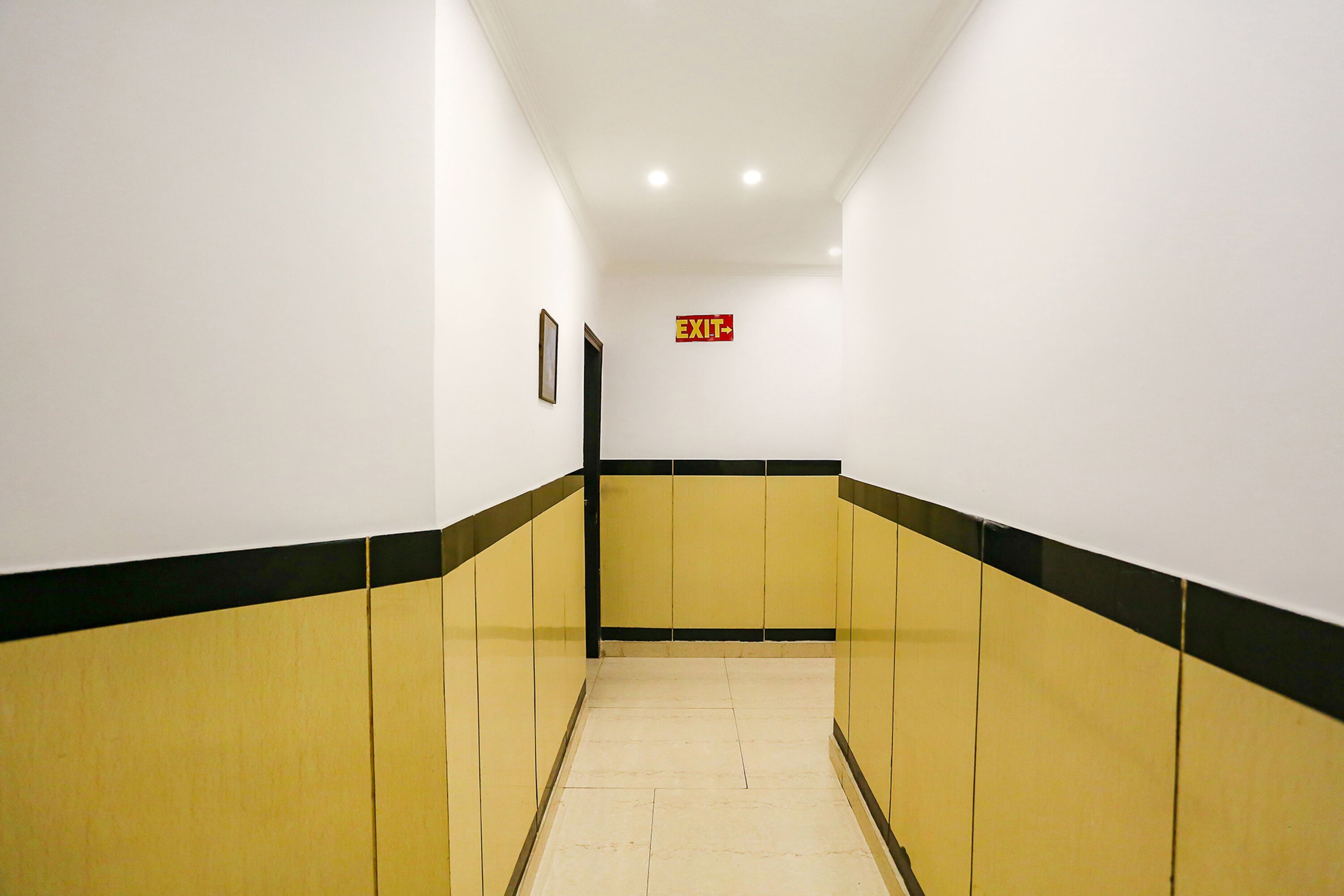 A hallway with yellow and black walls, a tiled floor, and an exit sign.