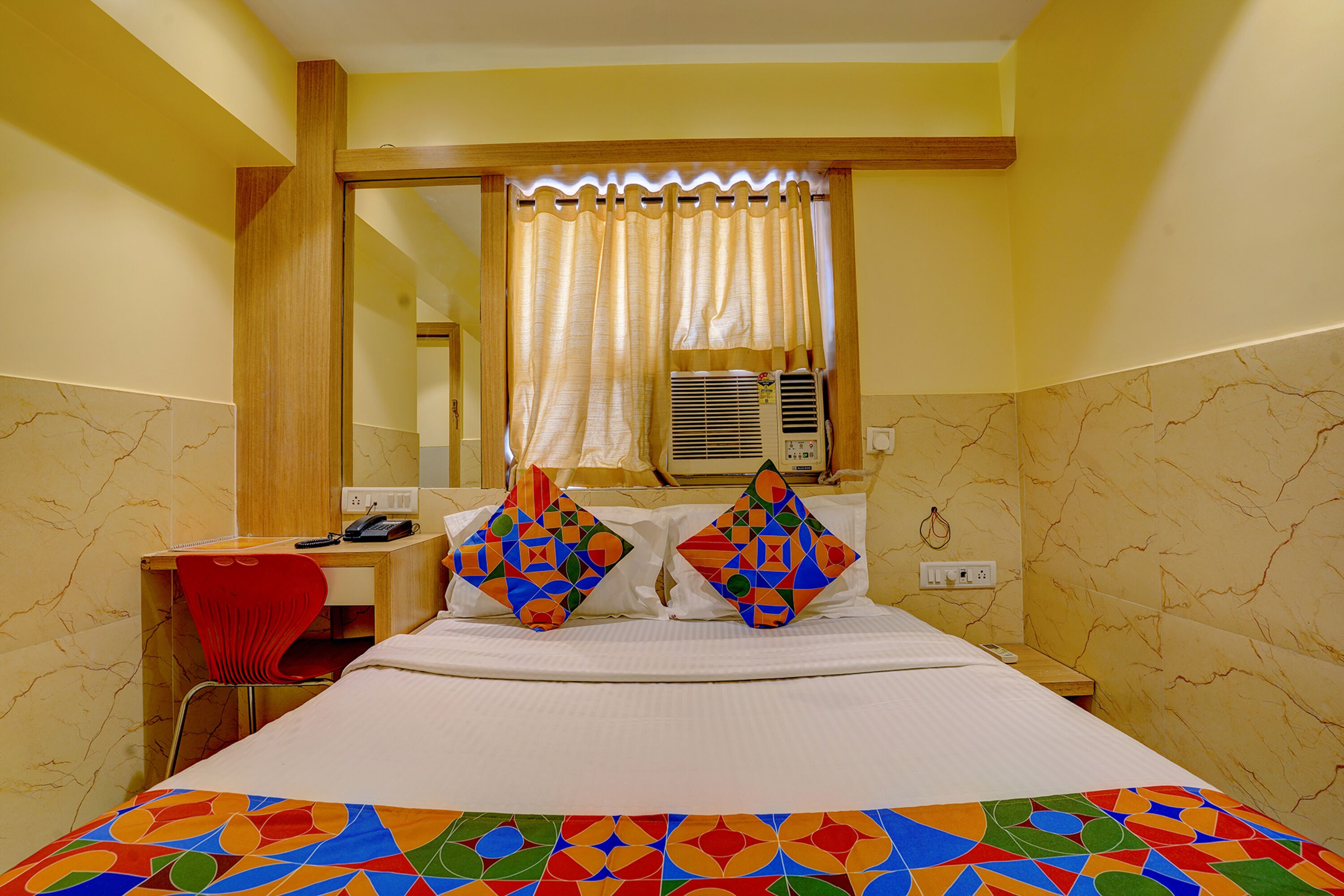 Habitación de hotel con cama, escritorio, silla y ventana con cortinas.