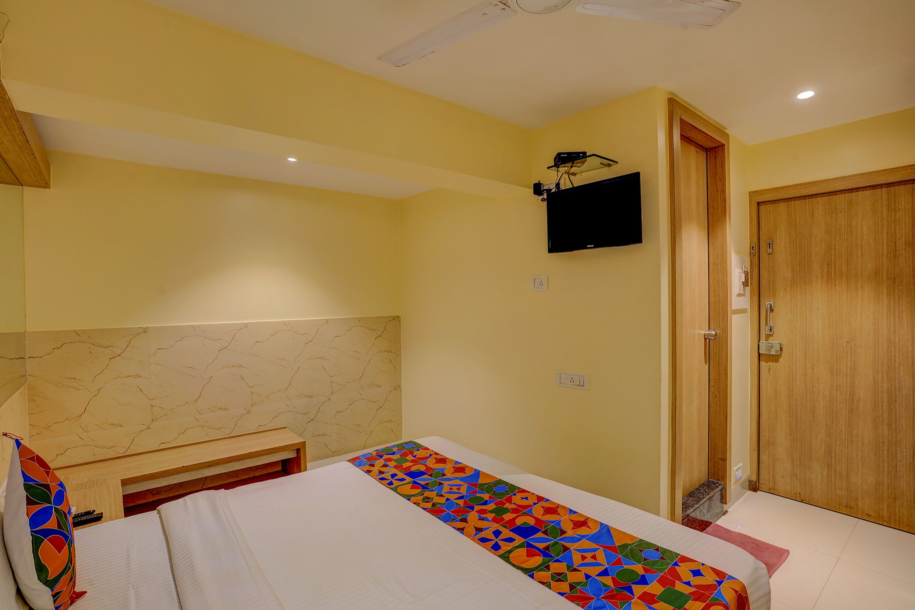 A hotel room with a bed, a television mounted on the wall, a wooden door, and a marble-patterned headboard.
