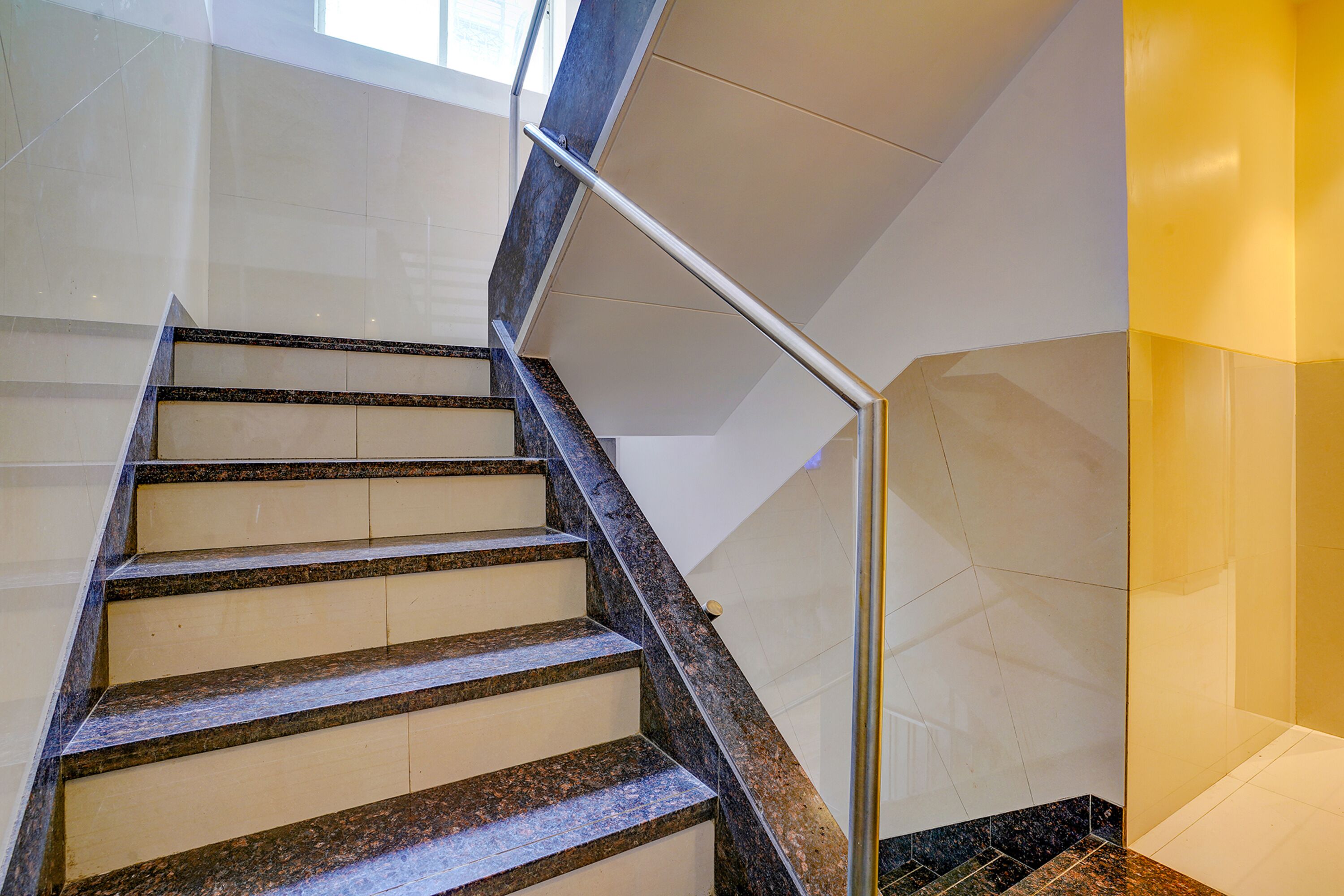 A staircase with a handrail and a corner with a yellow accent wall.