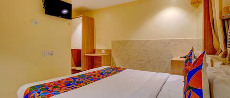 A hotel room with a bed, a ceiling fan, a TV mounted on the wall, and a wooden nightstand.
